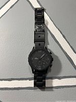 Single image of a black Fossil men's chronograph watch laying flat, showing black dial, stainless steel link bracelet with one pin missing.