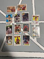 Photo showing 13 vintage hockey cards arranged in a grid on a light floor background, displaying players from various NHL teams including Flyers, Islanders, Blackhawks, and Sabres.