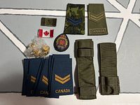 Lot of assorted Canadian military patches, pins, and fabric pouch holders arranged on a grey surface