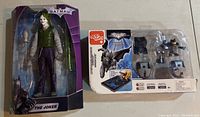 Joker action figure boxed with microphone stand and gun accessory alongside boxed Batman Batmobile toy set with mini-figures and components