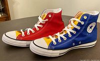 Side and top angle view of Converse Chuck Taylor high top sneakers showing one red and one blue shoe with yellow toe caps.