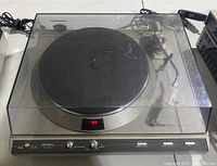 Full view of Denon Quartz DP-33F turntable with platter covered by clear plastic dust cover. Shows power switch, control panel with buttons and knobs, black platter, and tone arm visible through dust cover.