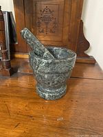 Side view of heavy stone mortar and pestle on wooden surface with wooden furniture background.