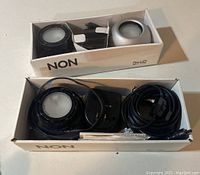 Set of Ikea NON series undercabinet lights and accessories in original box, showing black round light, mount, power adapter and cable.