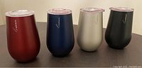 Front view of four stainless steel tumblers in red, navy blue, beige, and black with clear plastic lids and Rabbit branding.