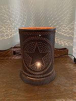 Front view of rustic punched tin light showing large star design pattern punched in metal with copper interior and glowing light center.