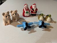 Front view of all salt and pepper shakers showing pig, dog, Mrs. Claus and Santa Claus, green birds, and blue airplanes