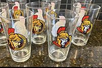 Four clear pint glasses with Ottawa Senators logo prominently displayed on front, arranged on dark granite counter.