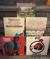 Photo of 5 vinyl record albums arranged on carpeted stairs showing front covers.