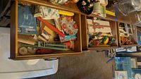 Top view of two wooden drawers and some surface area showing candles, flatware, playing cards, wax melts, and cocktail recipe booklets scattered inside, with some table cloths and small ornaments visible.