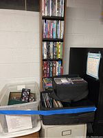 Wide view of assorted media collection showing white plastic bin with DVDs, black CD cases, and tall DVD shelf filled with DVDs