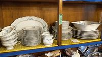Wide view showing stacked teacups, various plates, serving platter, and serving bowl on shelves