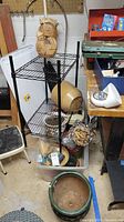 Black metal wire shelving unit with gardening items including planters, watering can, clothespins, and small step stool in basement