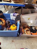 Photo showing blue storage bin containing orange jack-o-lanterns, haunted tree figurine, folded Halloween-themed towels, and black and orange polka dot fabric.