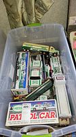 Plastic bin with several mixed Hess toy trucks and a boxed Hess Patrol Car toy.