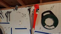 Pegboard with metal hooks and two bright orange Bluehawk ground stakes hanging on it, set in a wooden frame background.