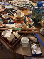 Photo showing a collection of kitchenware including Oneida plates, bowls, mugs, ceramic roosters, wooden tray, and assorted figurines on a table.