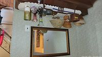 Photo showing the collection of items including the framed mirror, vintage lamp with floral shade, multiple woven baskets, pillar candles, and various decorative items along a wall.