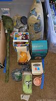 Overview of the lot items including boxed toys, plush toy, kitchen accessories, pillow and army men figurines arranged on carpet