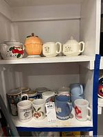 Shelf with various ceramic coffee mugs, sugar and creamer set, juicer bowl