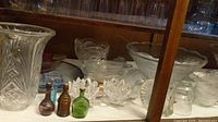 Clear pressed glass punchbowls, matching cups, small decorative glass bowls, and three miniature decorative glass bottles in amber and green.