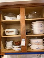 Wide shot of cupboard shelves showing various Pyrex and CorningWare casserole dishes in different patterns and shapes, stacked and organized.