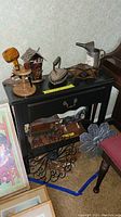 Shelf with drawer topped with various vintage decorative items including pipes on wooden stand, sad iron with trivet, horse and carriage display, and small wooden 'TOILET' hut.