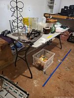 Full view of the folding table set up indoors, displaying various household and decorative items on top, including glassware, baskets, a decorative metal wine holder, and other miscellaneous objects.