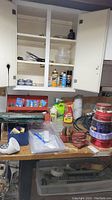 Photo of workbench surface and cabinet above showing assorted tools, tins, spray bottles, hose, and other items.
