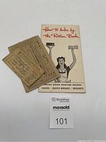 Photo of the cookbook and two ration cards laid out on a white surface with a MaxSold tag in view.