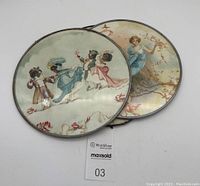 Shows two round decorative pieces stacked, exposing the Victorian African American dancing scene and the angelic figure. Glass covers and metal frames visible.