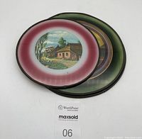 Top view showing three round stove pipe covers stacked, each with a glass-covered country scene graphic in pastel colors.