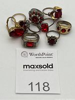 Photo showing 9 costume rings featuring varying sizes and designs of red stones on silver-tone metal bands, including different stone shapes and some cluster settings.