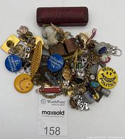 Lot overview with mixed small collectibles including jewelry, pins, novelty items, whistle, and small trinket case