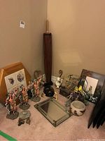 Overview of various decor items on carpeted floor including figurines of soldiers, frames, a vanity tray, small mirror, parasol, ceramic pot, and art pieces.