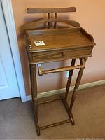 Front view of the wooden butler stand, showing drawer and hangers