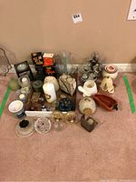 Overview of assorted candles, pottery, and decor items arranged on the floor including glass and ceramic pieces, candles, and decorative containers.