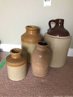 Set of four stoneware pieces: one large brown-handled jug, two matching stamped crocks and one plain brown crock on carpeted floor.