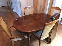 Full view of the oval wood dining table with four cane back chairs around it, showing wood finish and design.