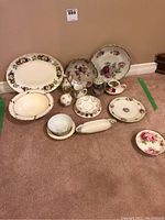 Photo showing assortment of dishes including various plates, bowls, cups, and platters all with floral patterns and gold trim on a carpeted floor.