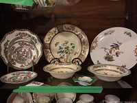 Assorted vintage porcelain dishes including plates and bowls with floral and bird designs arranged on shelf