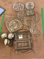 Top-down view of assorted clear glass serving dishes including divided plates and ashtray on a carpeted floor.
