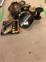 Lot showing small metal and glass oil lamp with metal holder, metal cauldron, black candle holder, small decorative metal plates, calligraphy set in box, and woven basket with lid.