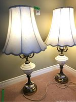 Pair of lamps shown with white fabric shades, featuring scalloped edges and brass bases with marble and frosted glass components.