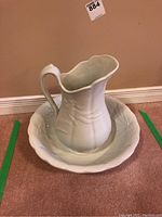 Full view of white pitcher and basin set on floor, showing shape and design