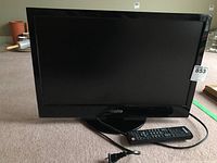 Front view of 22-inch Sanyo LED-LCD TV with remote on the floor showing screen and base stand.