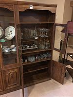 Front and side view of the pressboard wall unit showing glass doors, metal hardware, and shelves inside with glassware.