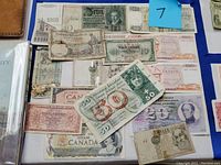 Photo showing a selection of worn foreign paper banknotes including Canadian dollars, Greek drachma, and others from Europe arranged on a flat surface with signs of use and aging.