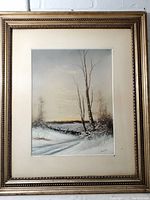 Framed pastel drawing showing winter landscape with snow, path, bare trees, and water under a soft sky.