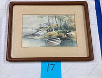 Full view of watercolor painting framed with matte and wooden frame showing lakeside cottage, small boats on shore, and trees